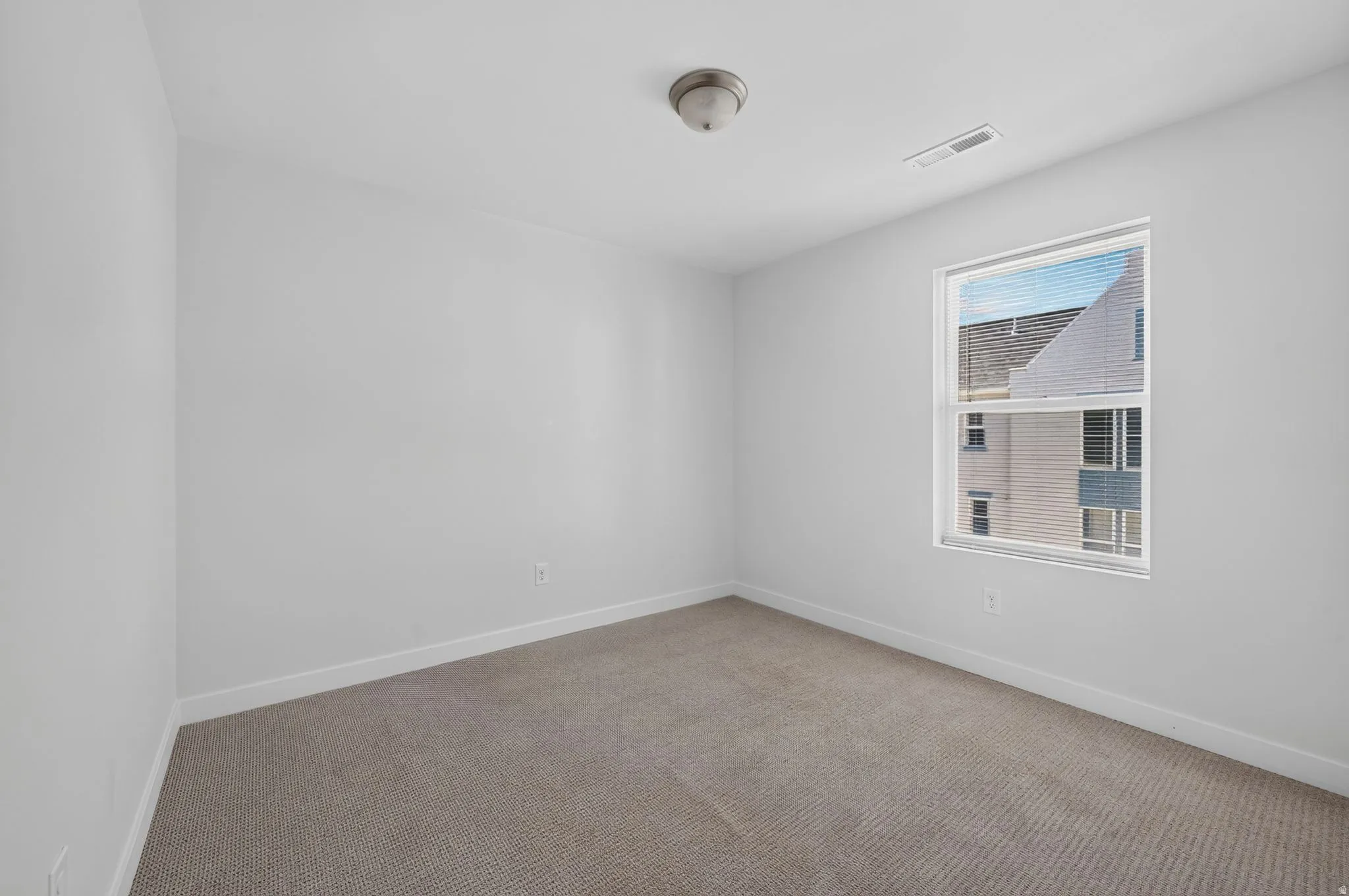Neutral tone wall paint, flush mount ceiling light fixture, single window with blinds, and carpeted flooring