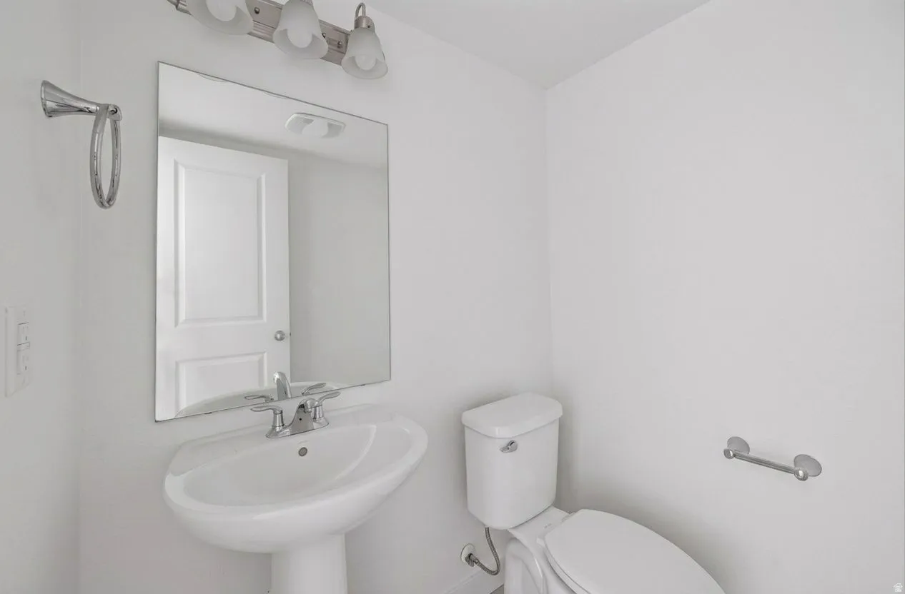 Pedestal sink with chrome faucet, wall-mounted mirror, and vanity light fixture