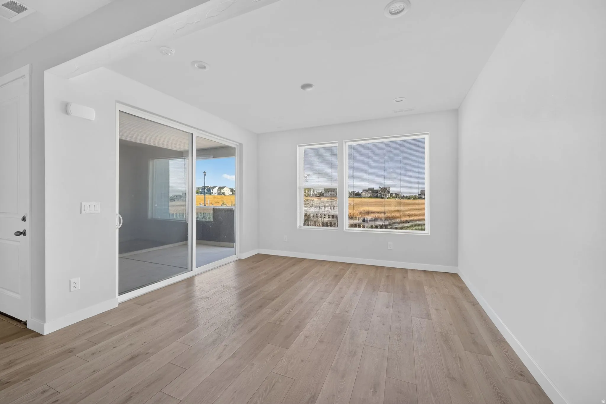 Recessed ceiling lighting, wood-finish flooring, white painted walls, double-paned windows, and a sliding glass door