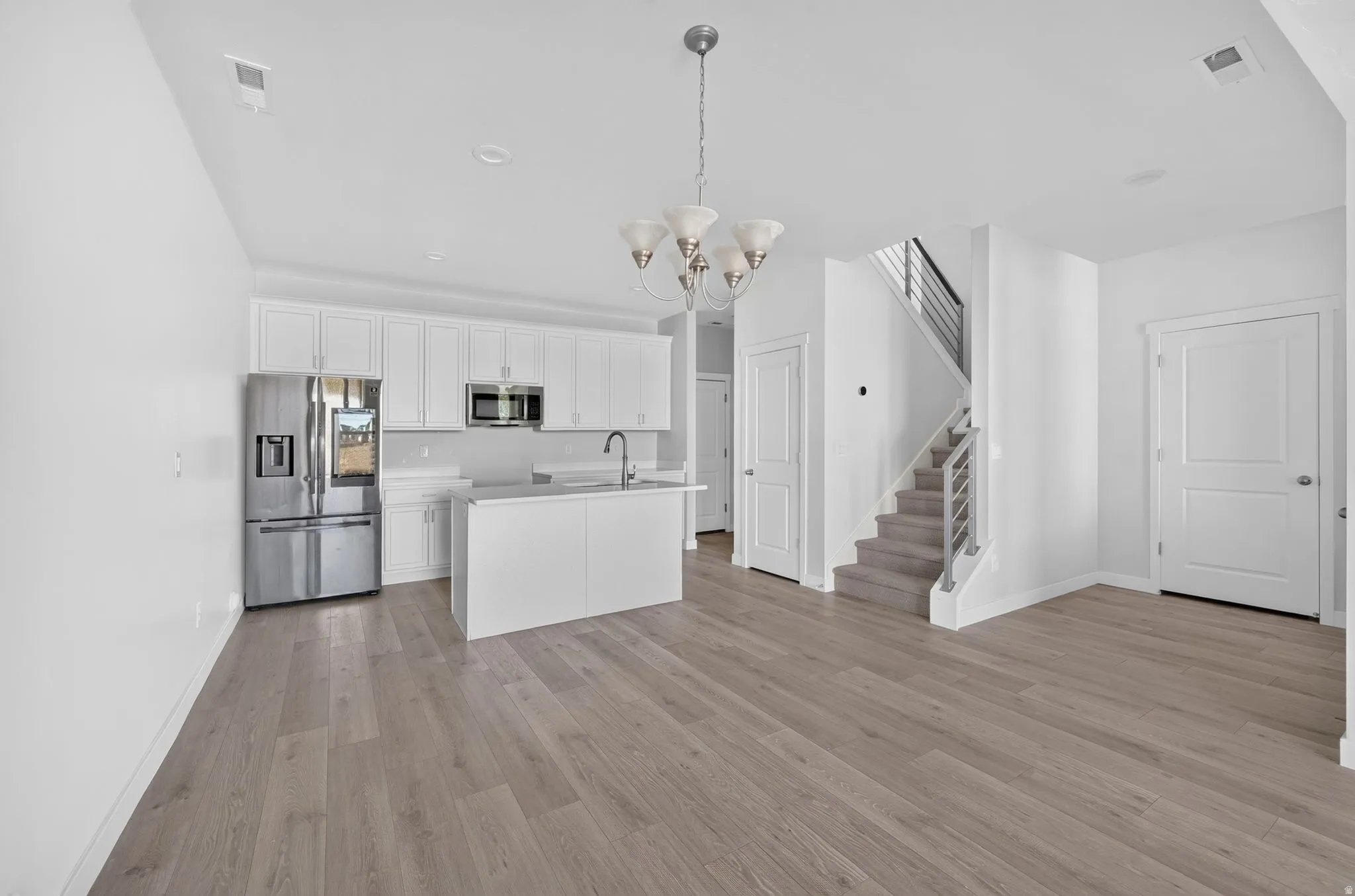 Modern kitchen featuring stainless steel appliances, white cabinetry, a kitchen island with an undermount sink, and wood-finish flooring