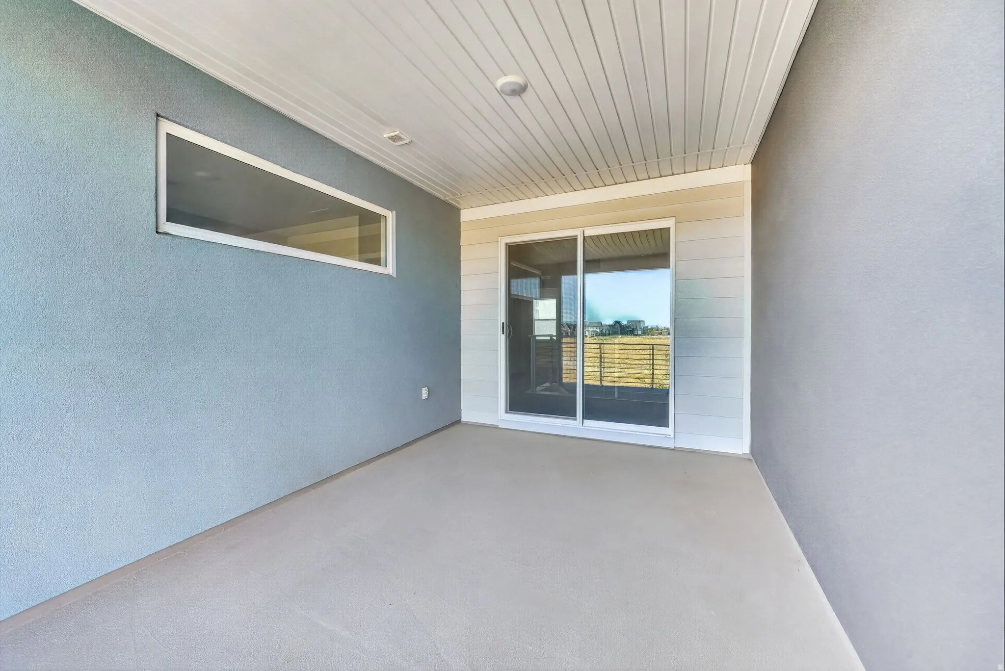 Covered outdoor patio with a concrete floor, horizontal window, and sliding glass door
