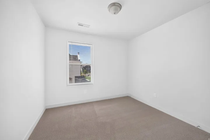 Neutral carpet flooring with white walls and a single window featuring blinds