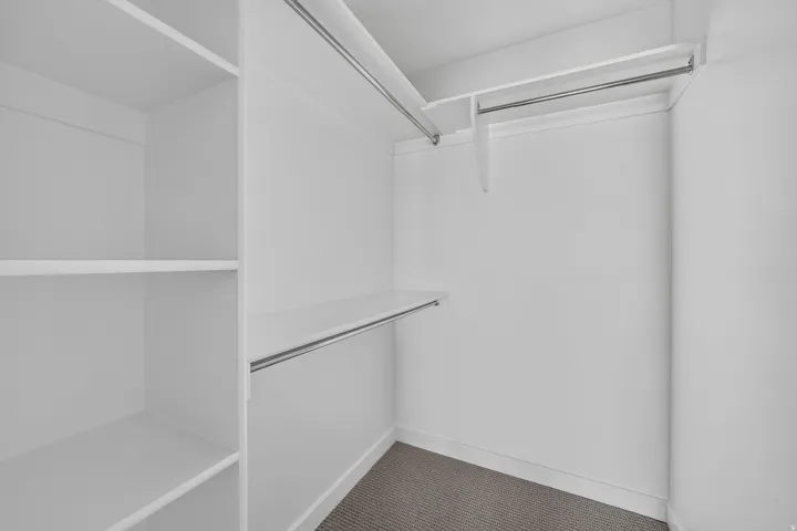 Built-in closet system with multiple shelves, two hanging rods, and neutral-toned carpeting