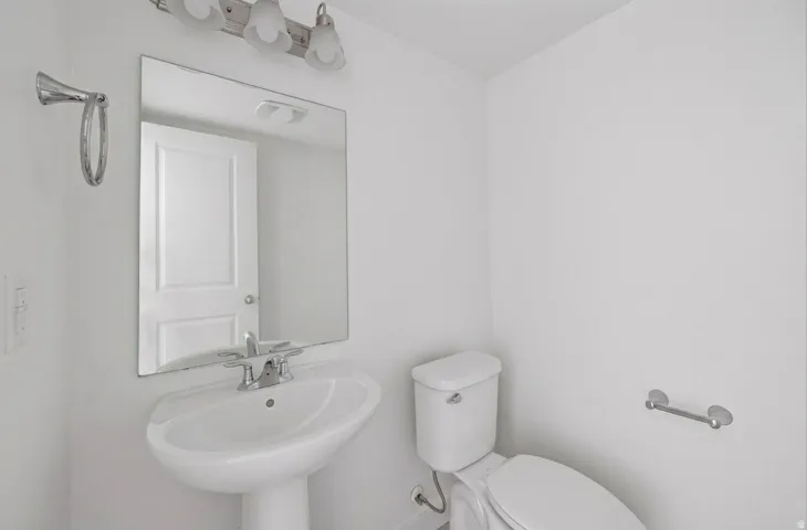 Pedestal sink with chrome faucet, wall-mounted mirror, and vanity light fixture