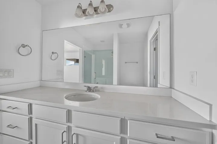 White vanity with recessed panel cabinet doors, integrated sink, chrome faucet, and expansive wall-mounted mirror