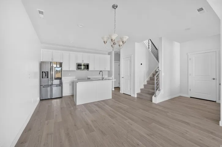 Modern kitchen featuring stainless steel appliances, white cabinetry, a kitchen island with an undermount sink, and wood-finish flooring