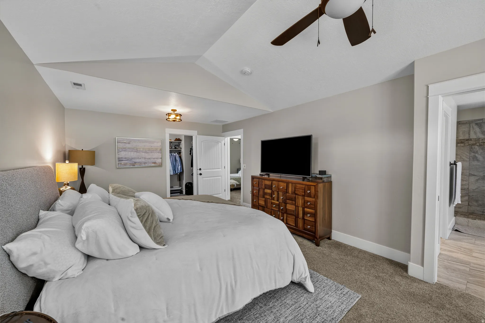 Tray ceiling, recessed lighting, ceiling fan, carpet flooring, and an open doorway to a tiled bathroom