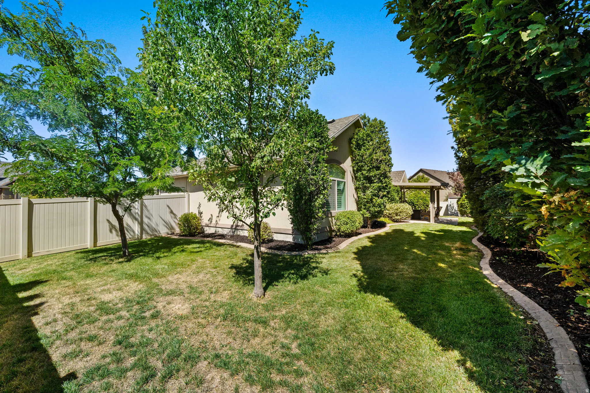 Expansive backyard featuring a manicured lawn, established trees, and perimeter fencing