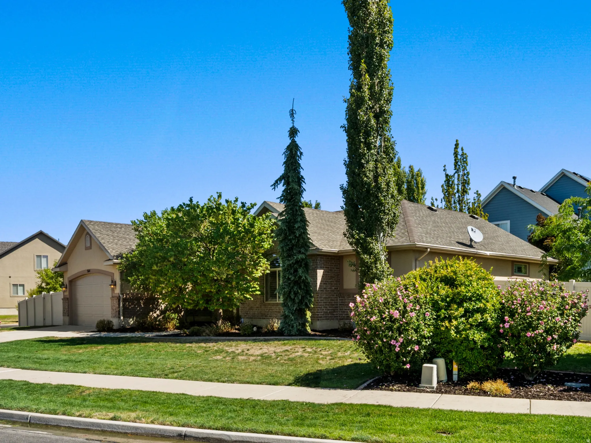 Manicured front yard with mature landscaping, a paved driveway, and an attached garage