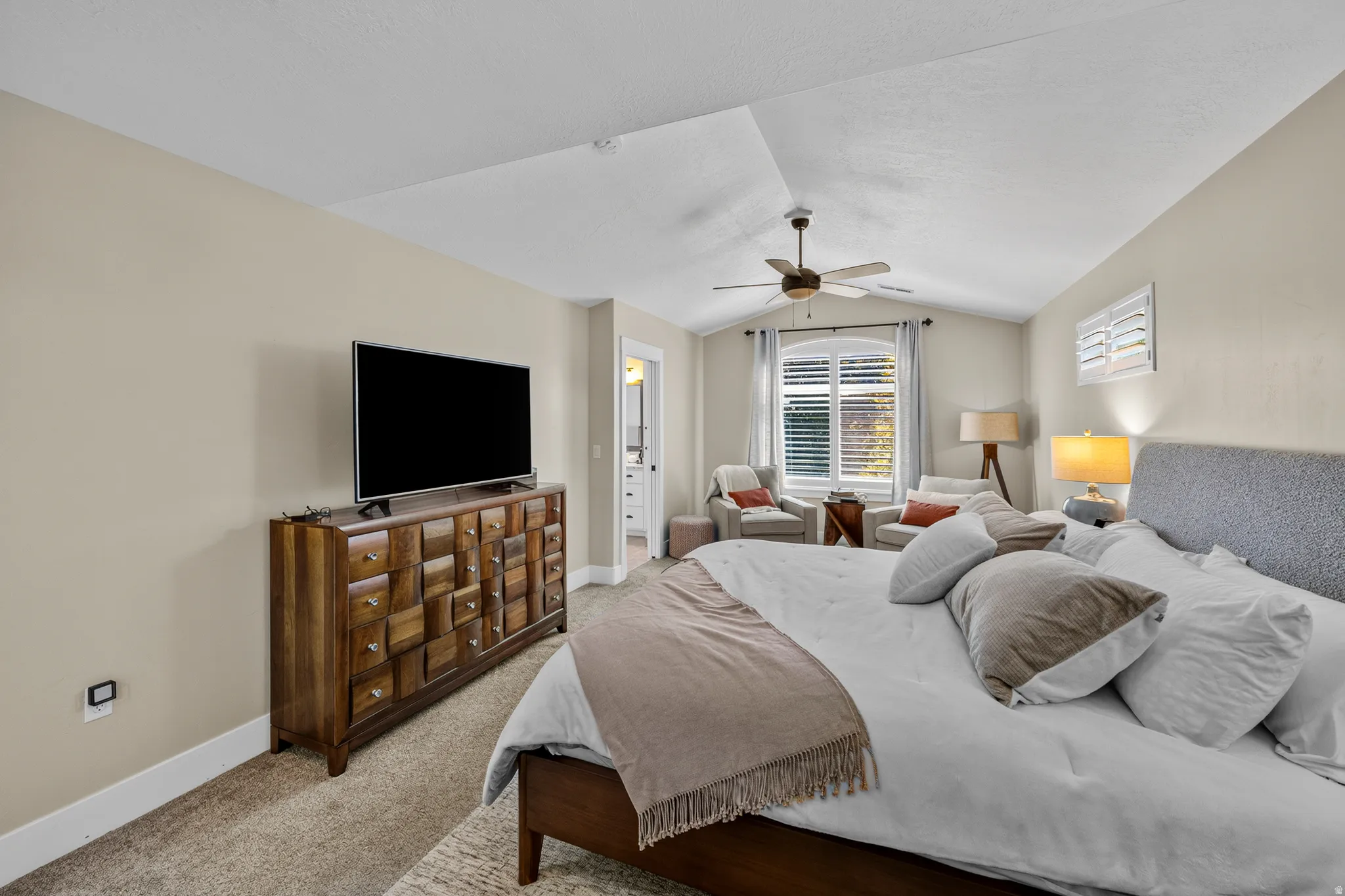 Vaulted ceiling with ceiling fan, large arched window, plantation shutters, and carpeted flooring