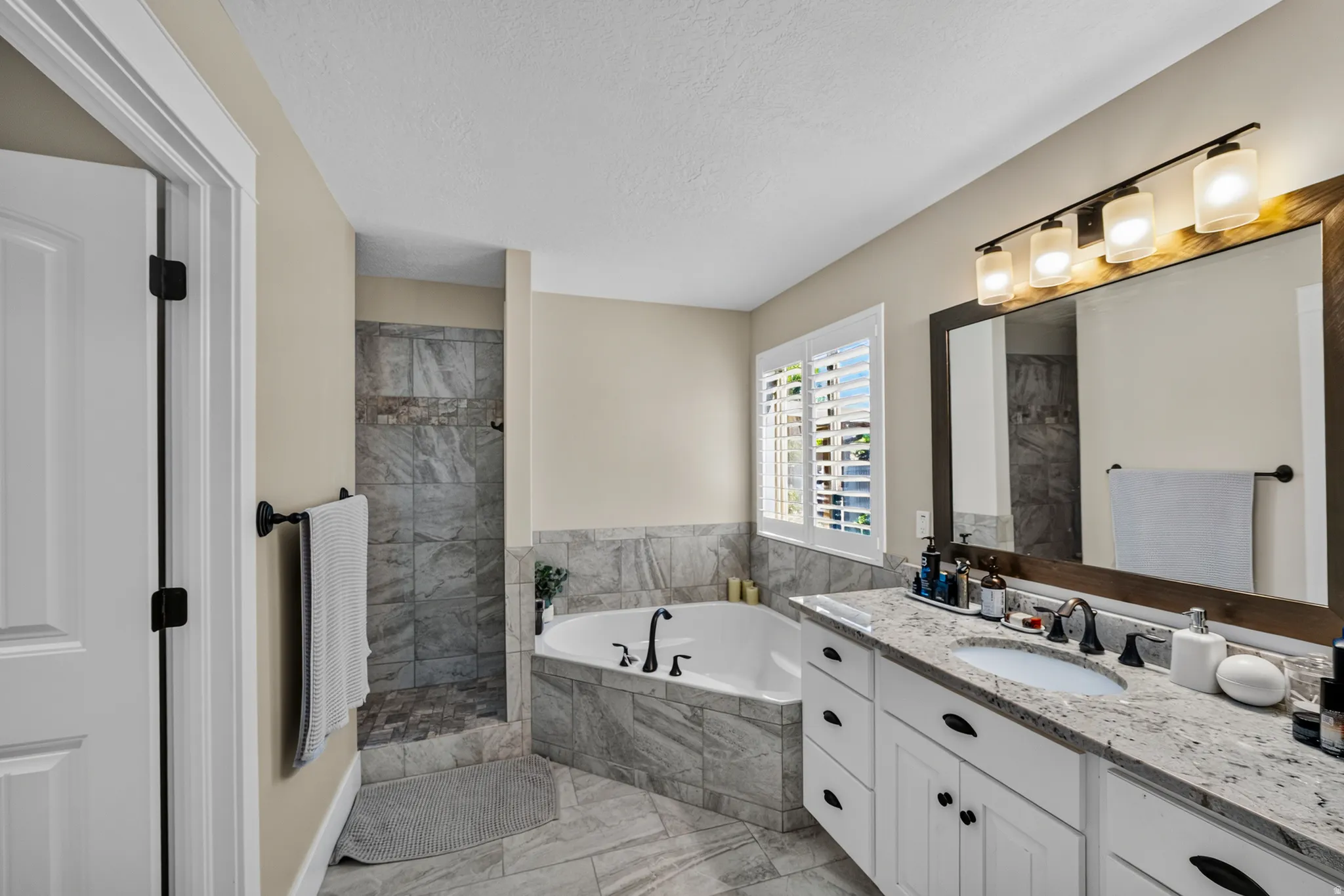 Spacious bathroom with a walk-in shower, soaking tub, and a vanity featuring a granite-style countertop and dual sinks