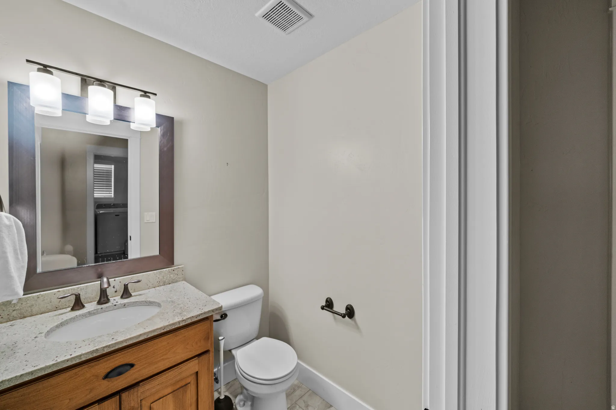 Wood-finish vanity with an undermount sink, light-toned countertop, and bronze-finish faucet