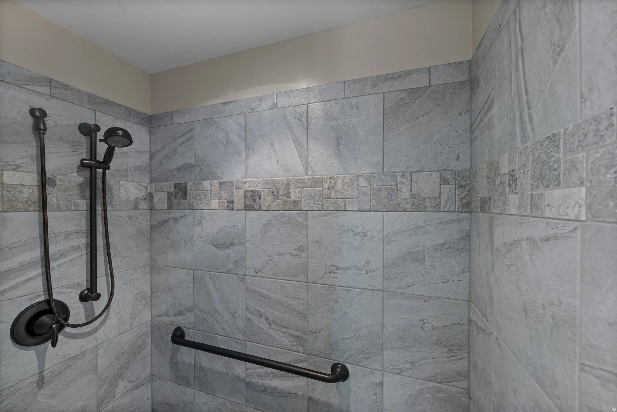 Tiled shower with a decorative mosaic accent band and dark bronze fixtures