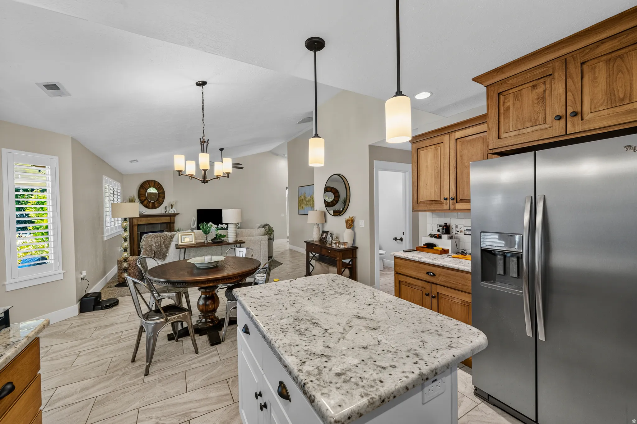 Kitchen featuring an island with a light-toned countertop, stainless steel refrigerator, wood-finish cabinetry, and pendant lighting