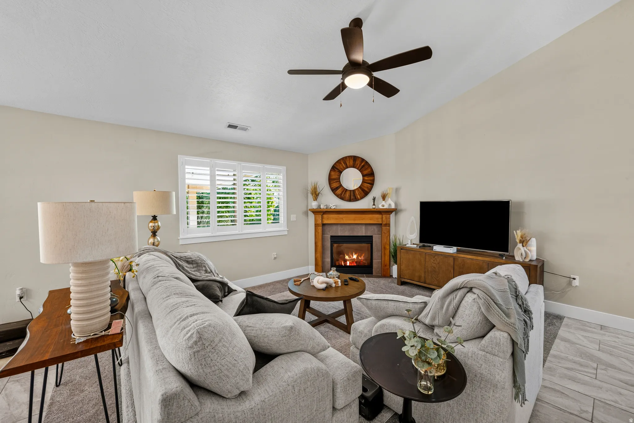 Carpeted living area with vaulted ceiling, ceiling fan, and window with plantation shutters