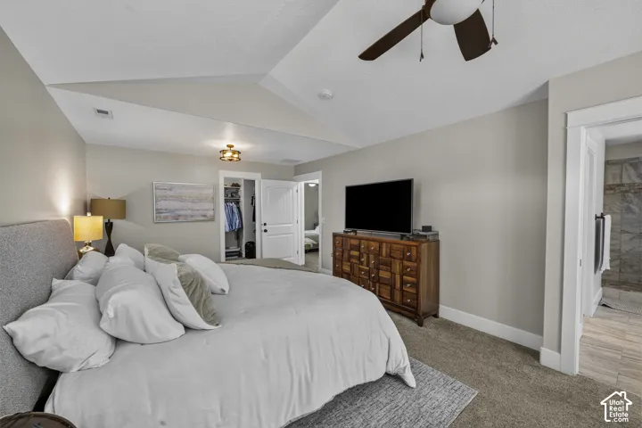 Tray ceiling, recessed lighting, ceiling fan, carpet flooring, and an open doorway to a tiled bathroom