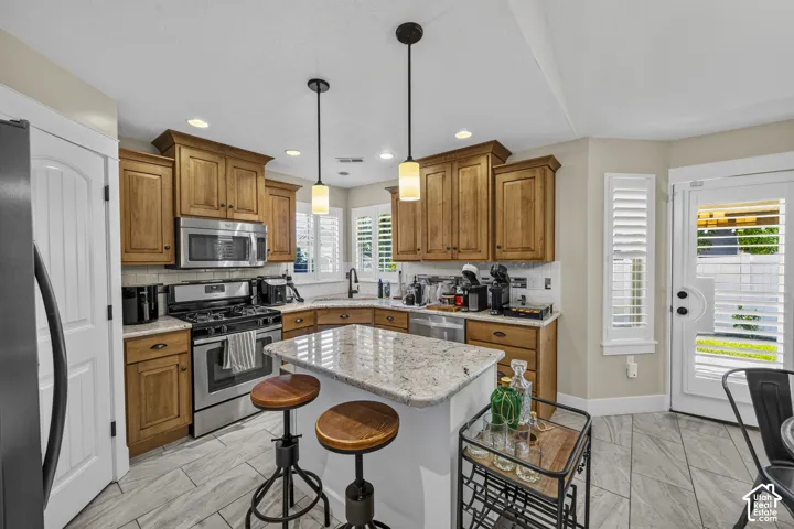 Full kitchen with wood cabinetry, stainless steel appliances, a corner sink, and an island with seating