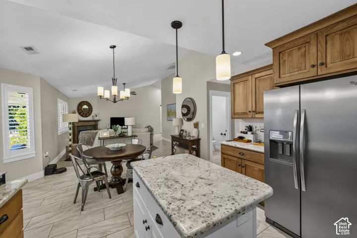 Kitchen featuring an island with a light-toned countertop, stainless steel refrigerator, wood-finish cabinetry, and pendant lighting