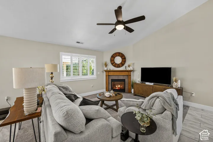 Carpeted living area with vaulted ceiling, ceiling fan, and window with plantation shutters