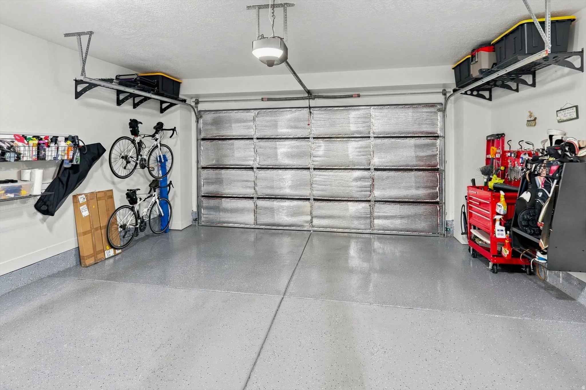 Garage featuring an insulated door, overhead storage racks, wall-mounted storage shelving, and an epoxy-coated concrete floor