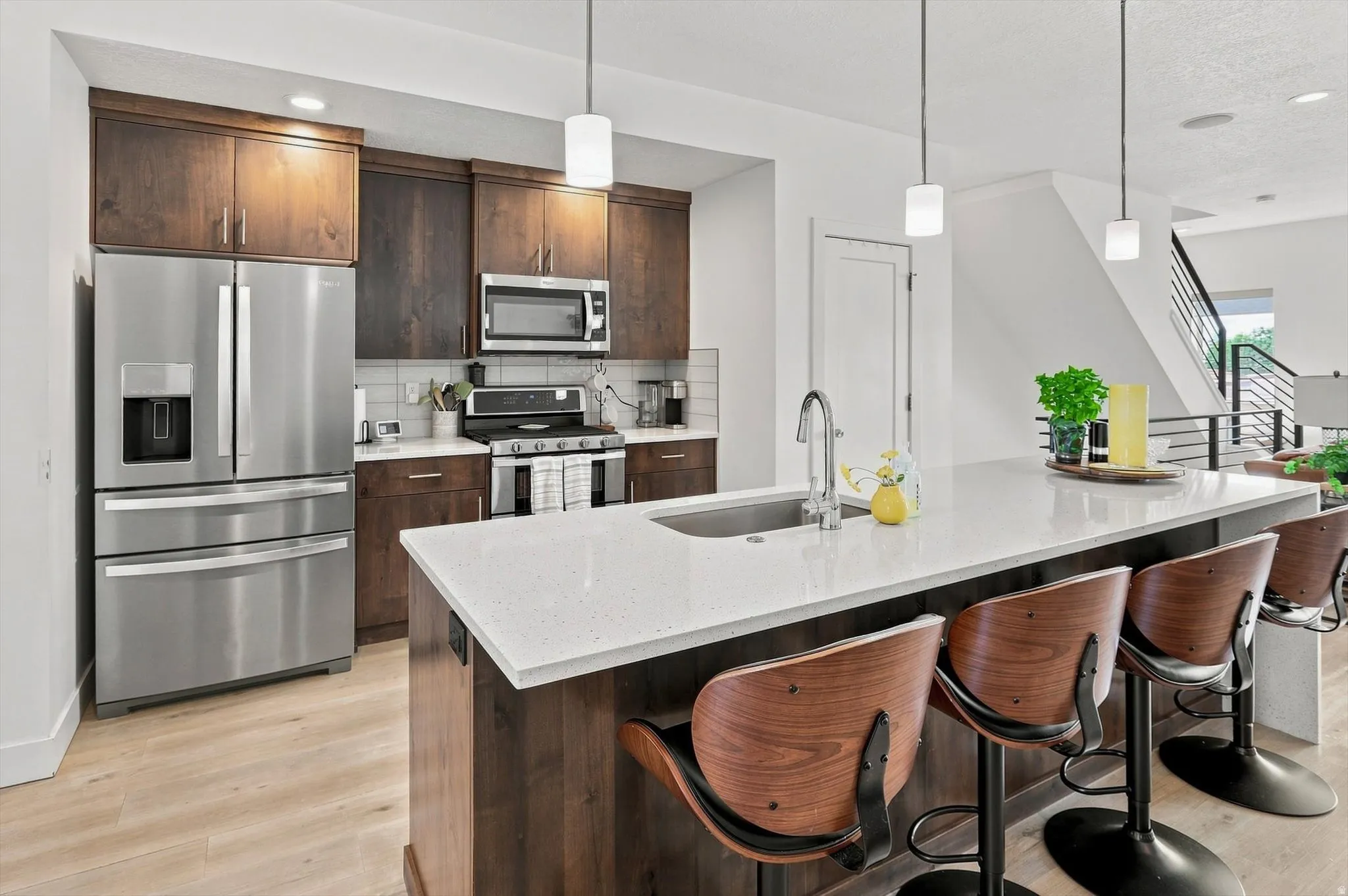 Kitchen featuring stainless steel appliances, dark wood-finish cabinetry, light-toned countertops, a kitchen island with an integrated sink, and wood-finish flooring