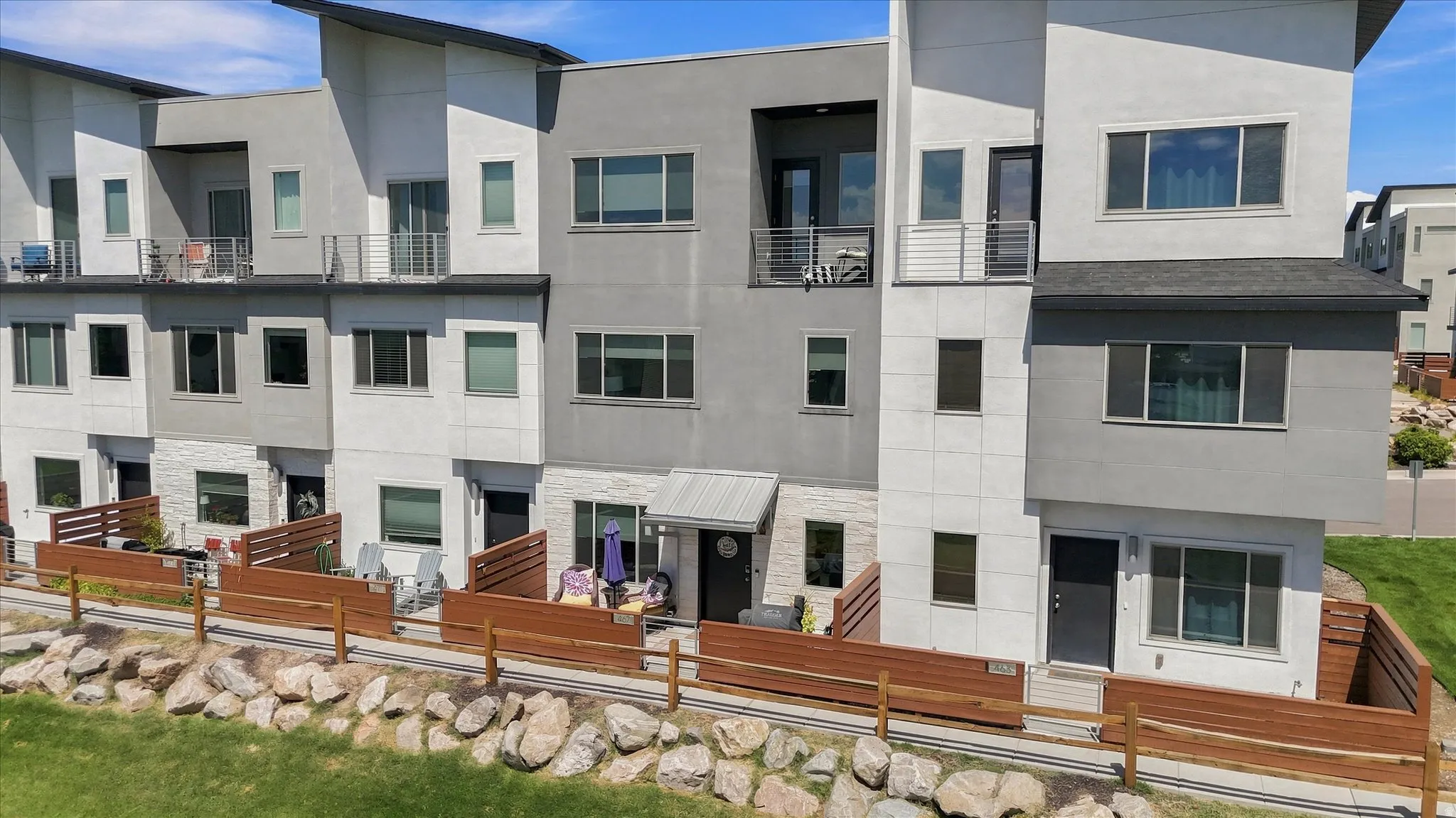 Multi-level townhome featuring a neutral-toned exterior, multiple private patios, and upper-level balconies with metal railings