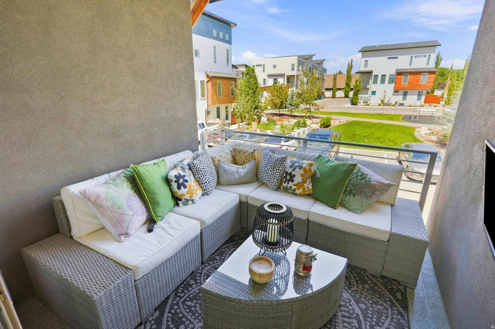 Outdoor balcony with a glass and metal railing, textured stucco wall, and a geometric pattern rug