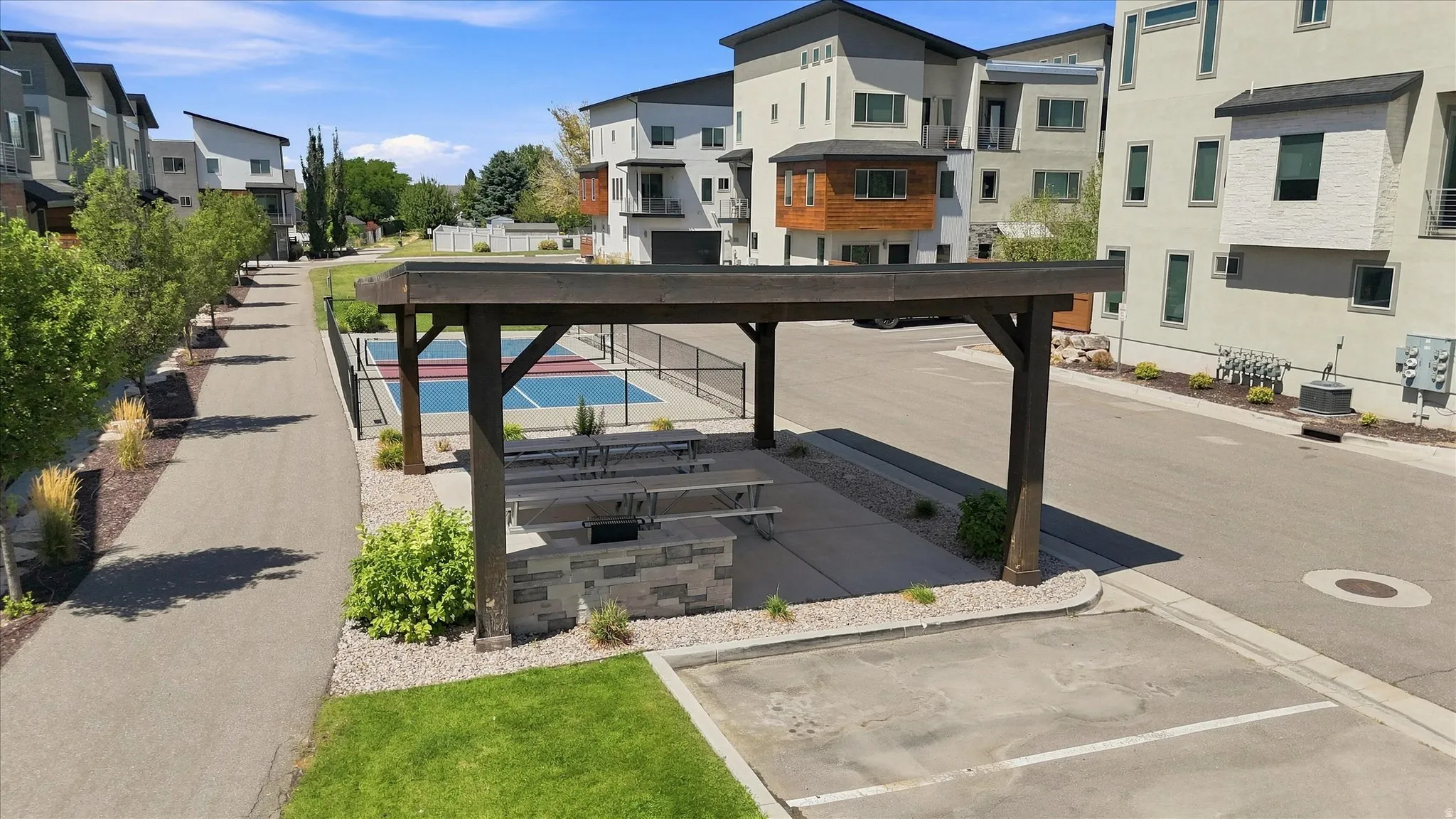 Outdoor pavilion with built-in barbecue station and picnic tables, adjacent to a hard-surfaced sport court