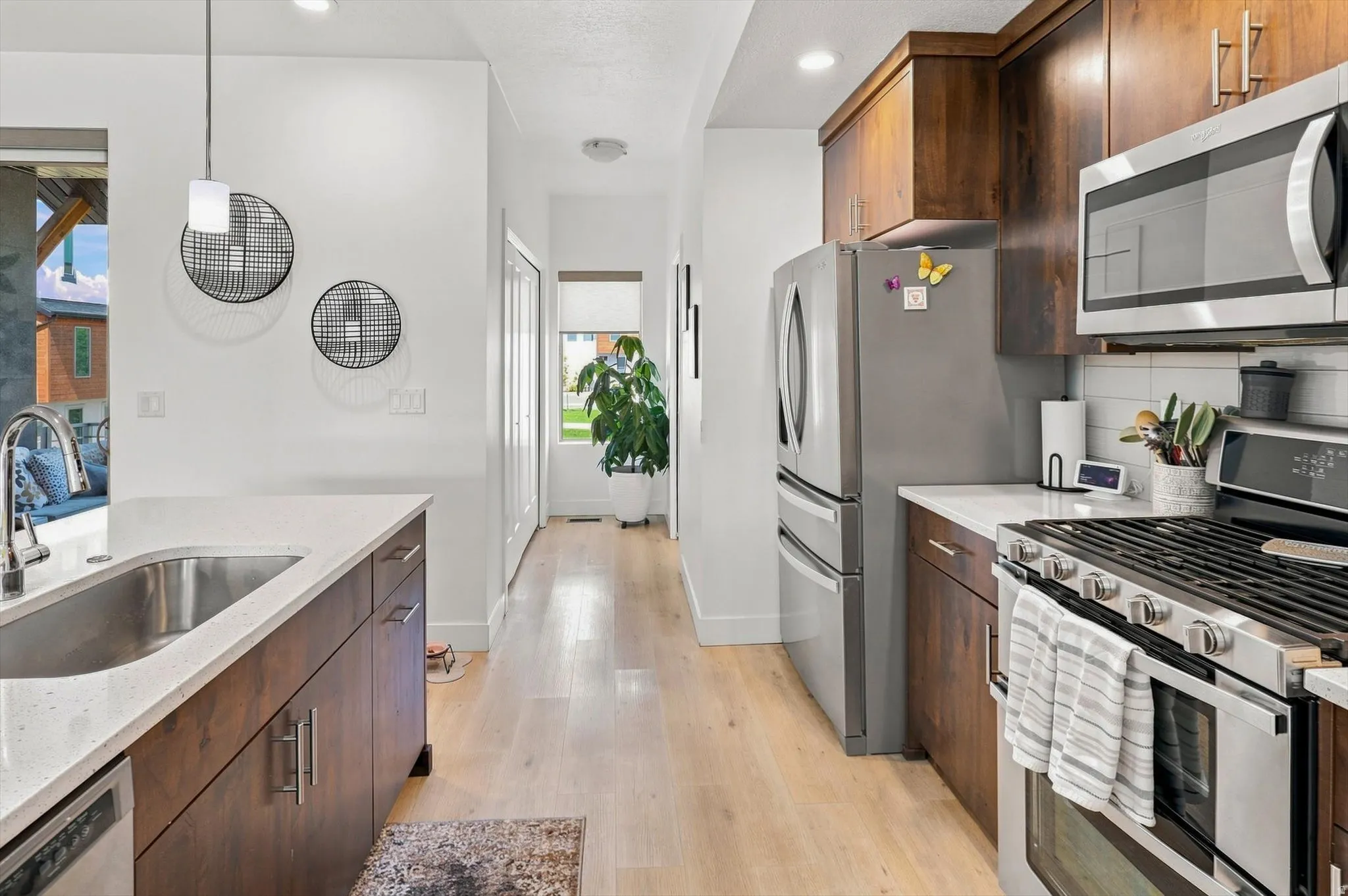 Kitchen featuring stainless steel appliances, wood-finish cabinetry, light-toned wood-finish flooring, and a stone countertop with an undermount sink