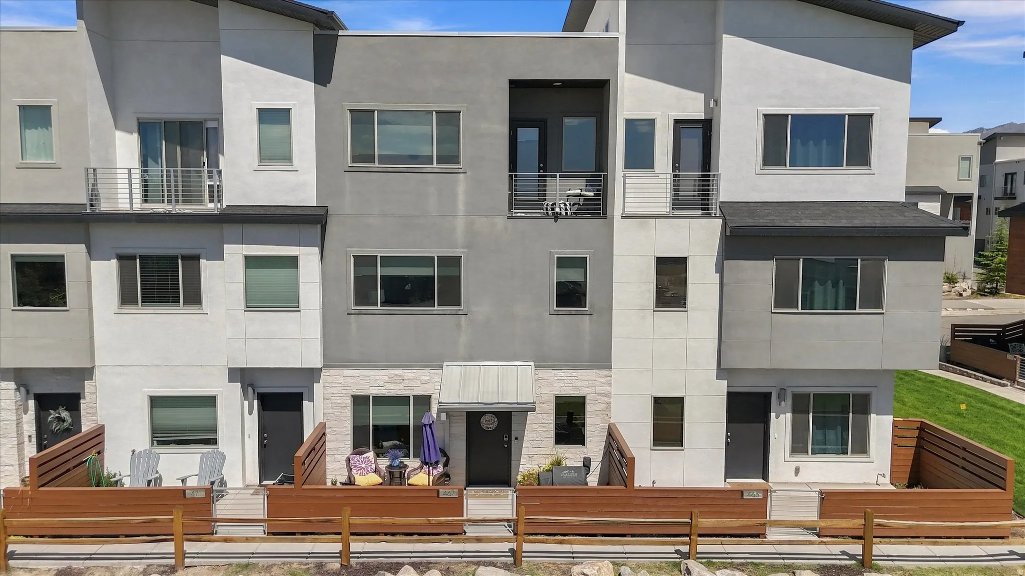 Modern multi-level townhome featuring a mix of stucco and stone-look siding, multiple balconies with metal railings, and a covered entry with a contemporary awning