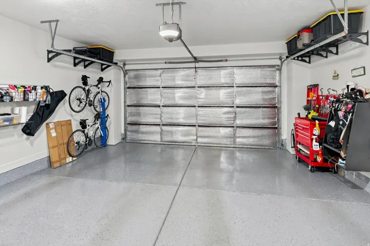 Garage featuring an insulated door, overhead storage racks, wall-mounted storage shelving, and an epoxy-coated concrete floor