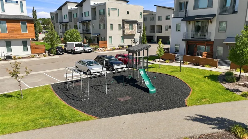 Grassed common area featuring a playground with a slide and monkey bars, bordered by landscaped shrubs and a paved walkway