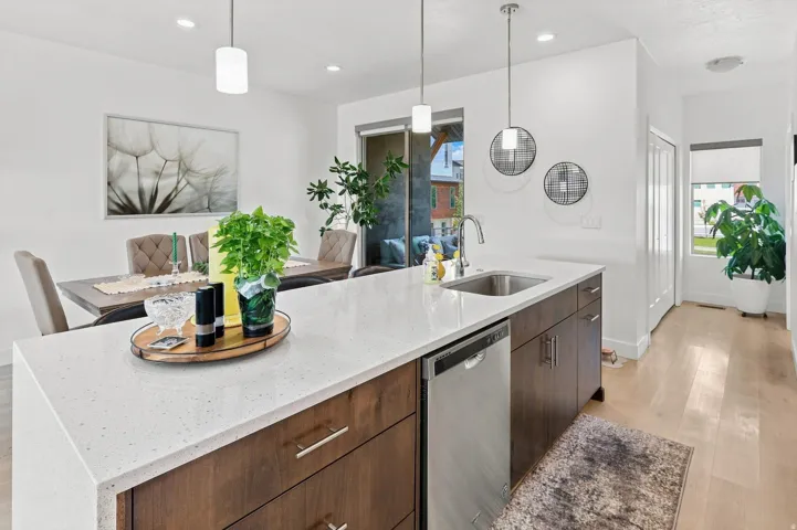Kitchen island with a light-toned countertop, integrated stainless steel sink, and a built-in dishwasher