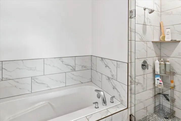 Soaking tub with chrome fixtures, surrounded by white and gray veined tile
