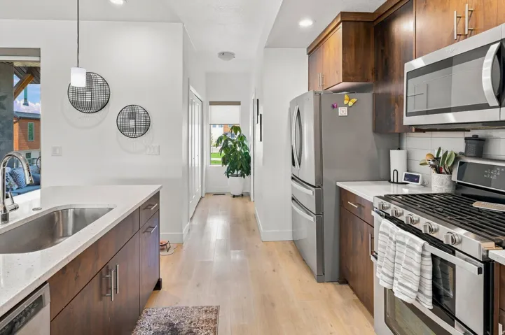 Kitchen featuring stainless steel appliances, wood-finish cabinetry, light-toned wood-finish flooring, and a stone countertop with an undermount sink