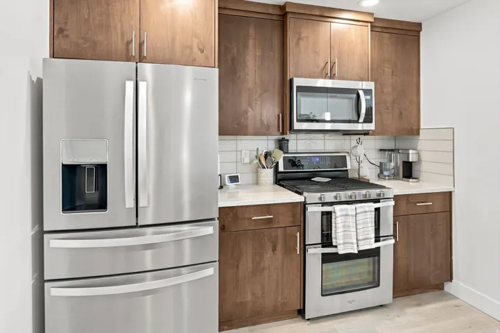Stainless steel French door refrigerator, wood-finish cabinetry, stainless steel microwave, stainless steel range with double ovens, and light-toned countertops