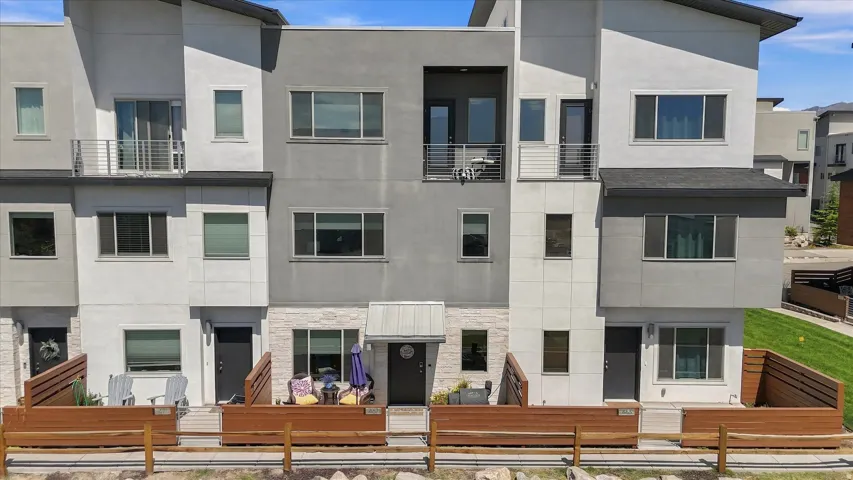Modern multi-level townhome featuring a mix of stucco and stone-look siding, multiple balconies with metal railings, and a covered entry with a contemporary awning