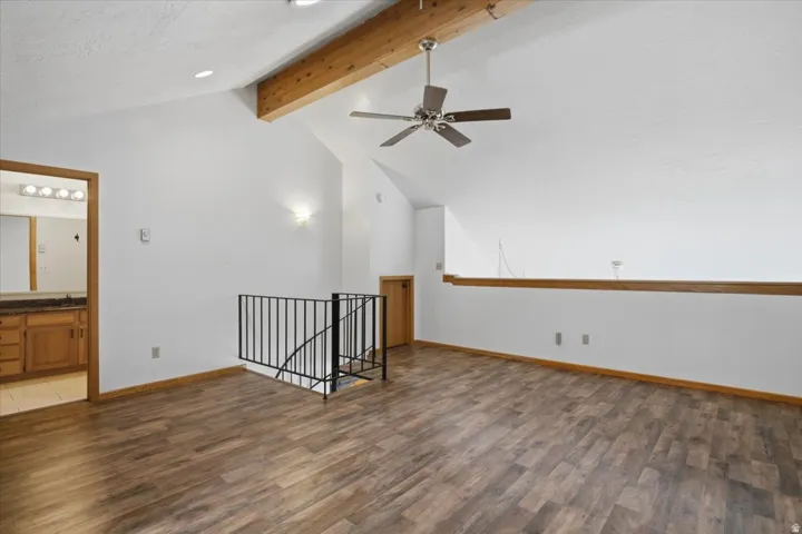 Vaulted ceiling with exposed wood beam, wood-finish flooring, ceiling fan, and wrought iron railing