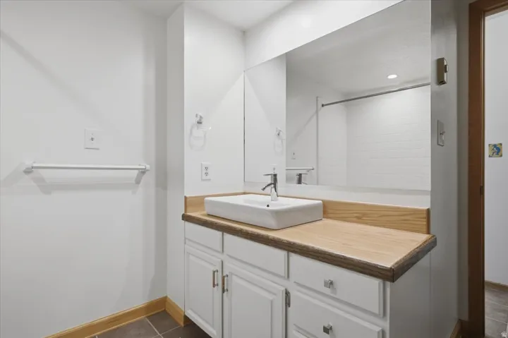 Bathroom featuring a rectangular vessel sink, wood-finish countertop, white cabinetry, and tiled flooring