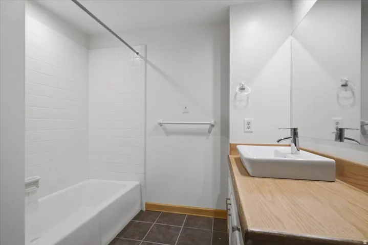 Bathtub with subway tile surround, wood-finish countertop, vessel sink, and large wall-mounted mirror