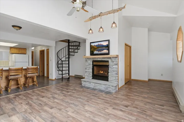 Vaulted ceilings, wood-finish flooring, stone-clad fireplace with wood mantel, spiral staircase, and a wood-panel kitchen island with countertop
