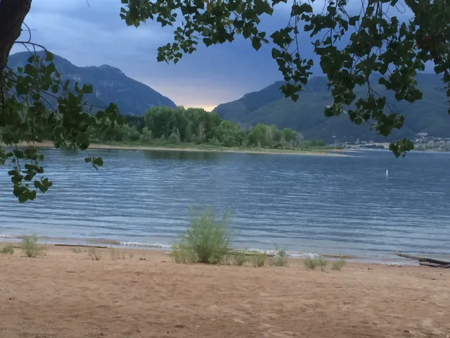 Sandy shore with tranquil waters, framed by distant mountains and lush trees