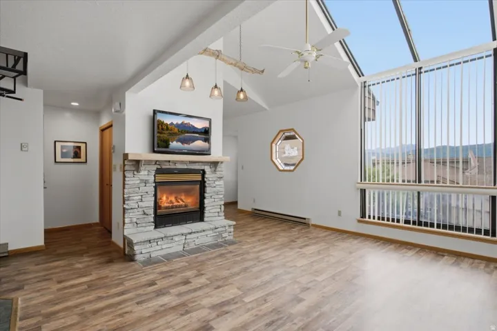 Stone-faced fireplace with a hearth, wood-finish flooring, vaulted ceiling, and expansive windows