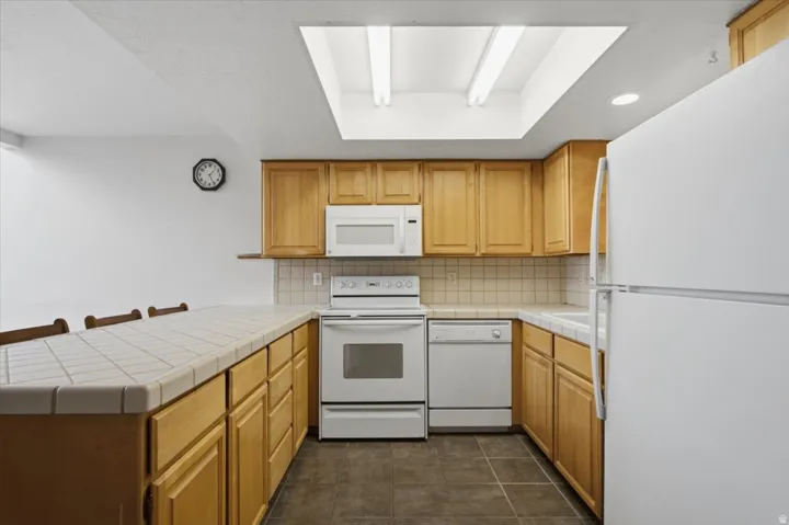 Kitchen featuring light wood-finish cabinetry, tile countertops, recessed lighting, and a skylight