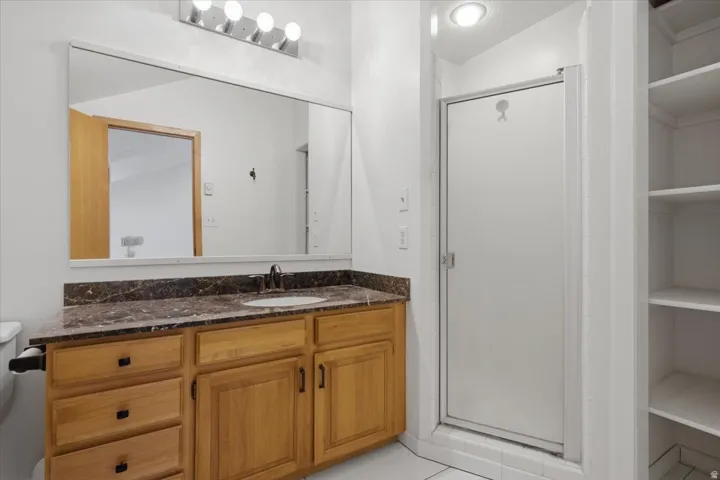Wood-finish vanity with a stone-finish countertop, single basin sink, and wall-mounted mirror