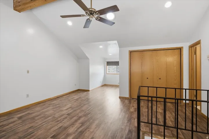 Vaulted ceiling with exposed wood beam, wood-finish flooring, recessed lighting, and a ceiling fan