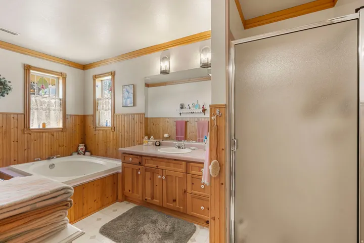 Built-in soaking tub, wood paneling, wood-finish vanity with integrated sink, and a frosted glass shower enclosure