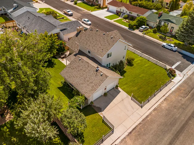 Pitched asphalt shingle roof, two-car attached garage, expansive green lawn, concrete driveway, and white picket fencing