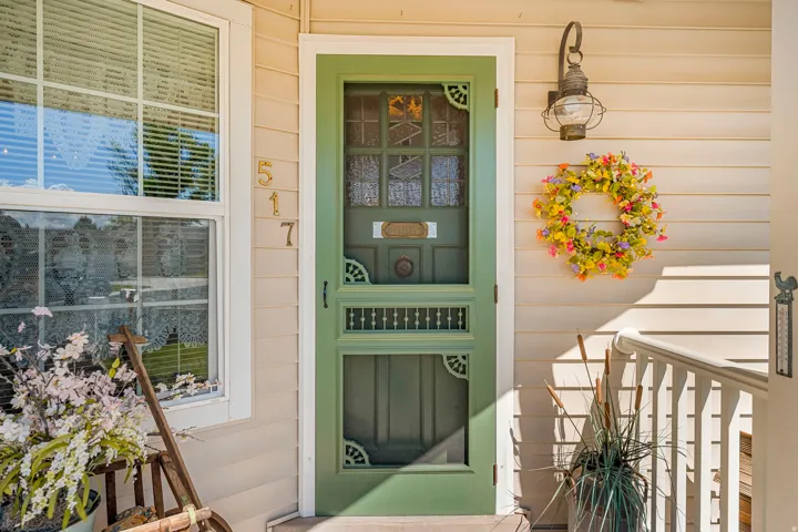 Front entrance featuring a green screen door, cream horizontal siding, white trim, and an exterior wall lantern