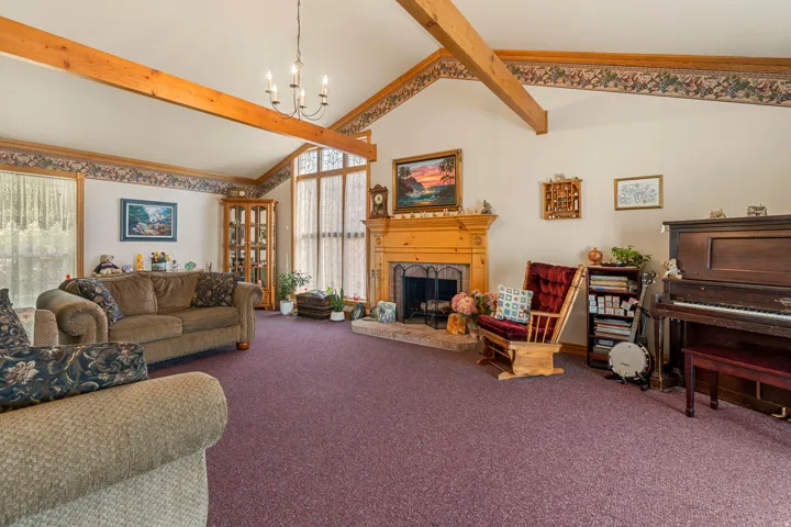 Vaulted ceiling with exposed wood beams, wood-mantled fireplace, and large window array